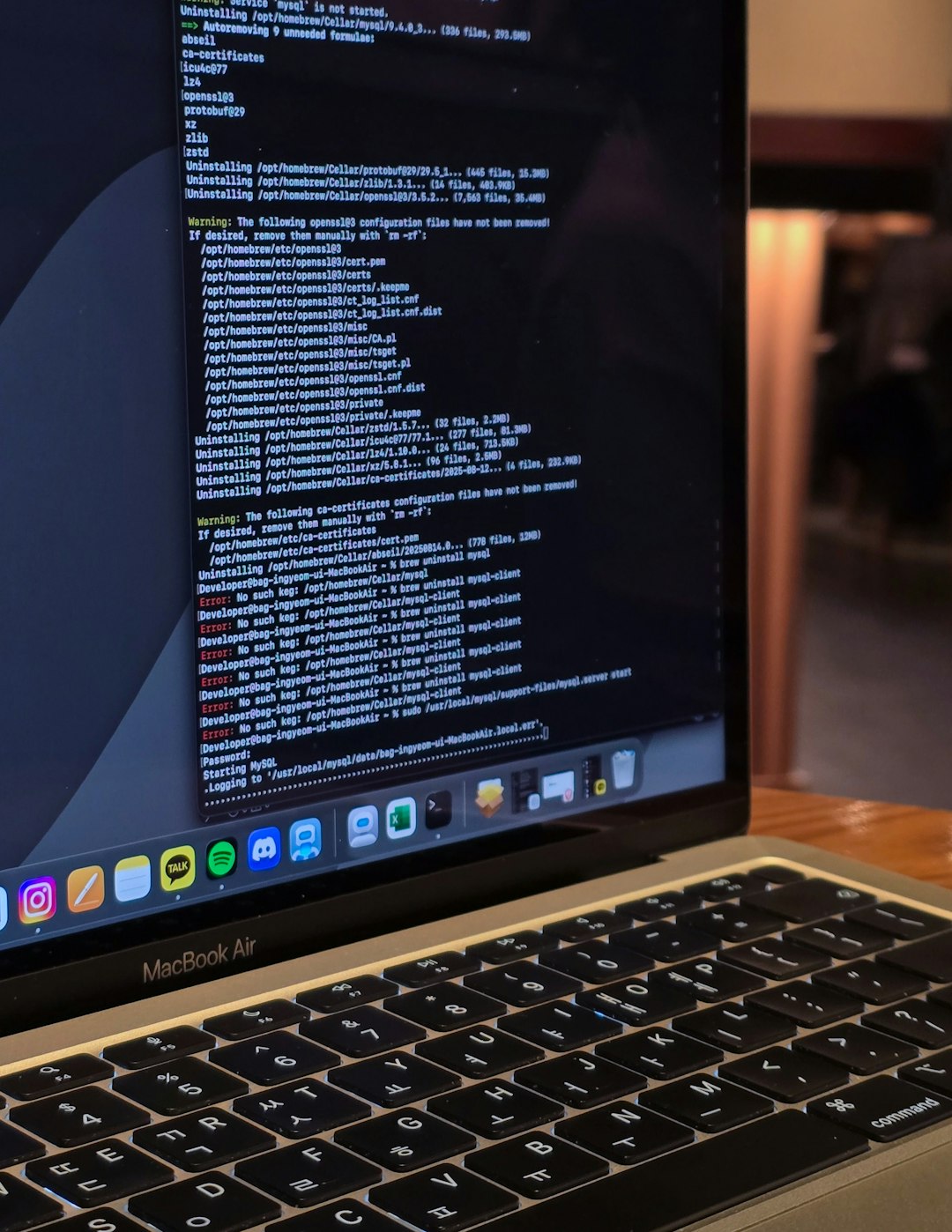 Close-up of a MacBook Air displaying terminal commands and code logs in a cozy indoor workspace with warm ambient lighting, capturing a developer’s workflow.